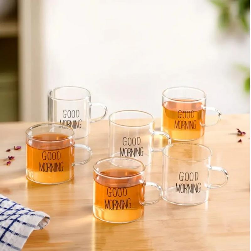 Clear glass mugs with 'Good Morning' text filled with a warm beverage on a wooden surface.