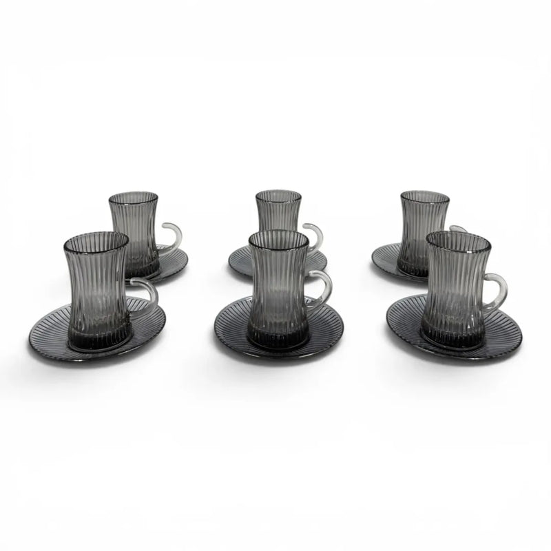 A complete 12-piece smoky grey glass tea service set showing six vertical ribbed glasses with handles sitting on their matching fluted saucers on Spotngrab Lebanon.