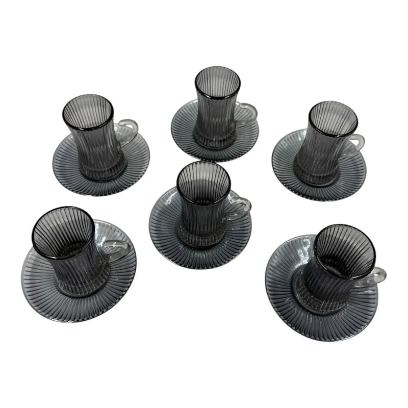 A complete 12-piece smoky grey glass tea service set showing six vertical ribbed glasses with handles sitting on their matching fluted saucers on Spotngrab Lebanon.