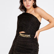 A woman wearing a black one-shoulder mini dress with a gold-colored belt.
